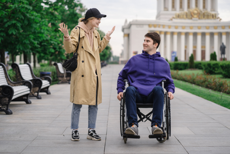 Two friends talking in the park, one in a wheelchair, sharing a joyful moment together