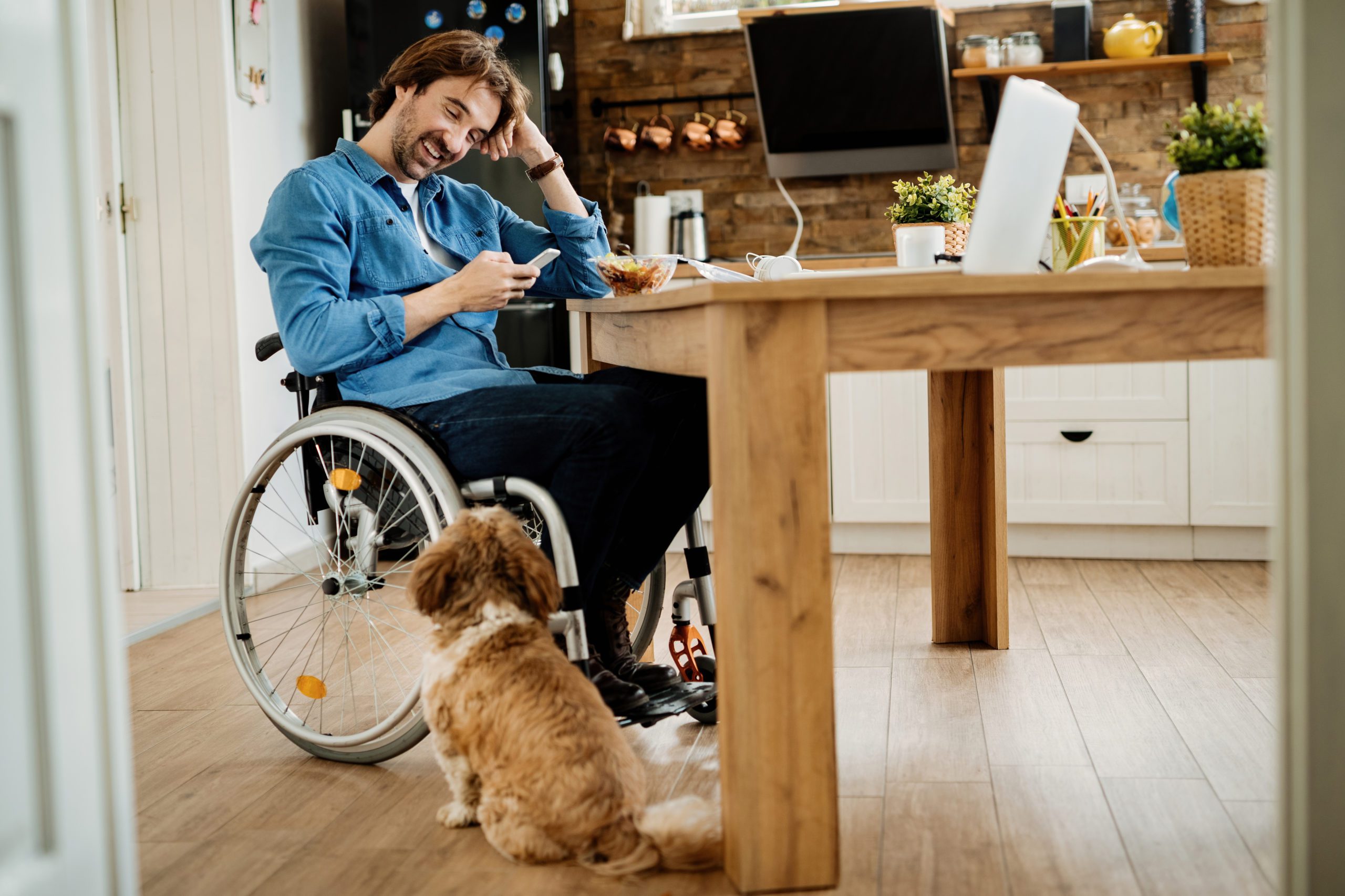 Happy disabled businessman using mobile phone while taking a break from work at home. man in wheelchair sitting at table and looking at mobile phone