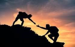 A hiker reaches out their hand to help another hiker up a hill.
