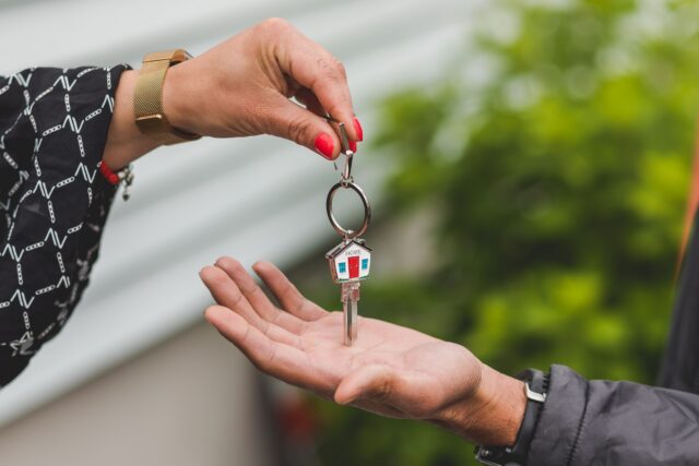 Close-up of a hand handing over a key with a house keychain, symbolizing real estate transaction