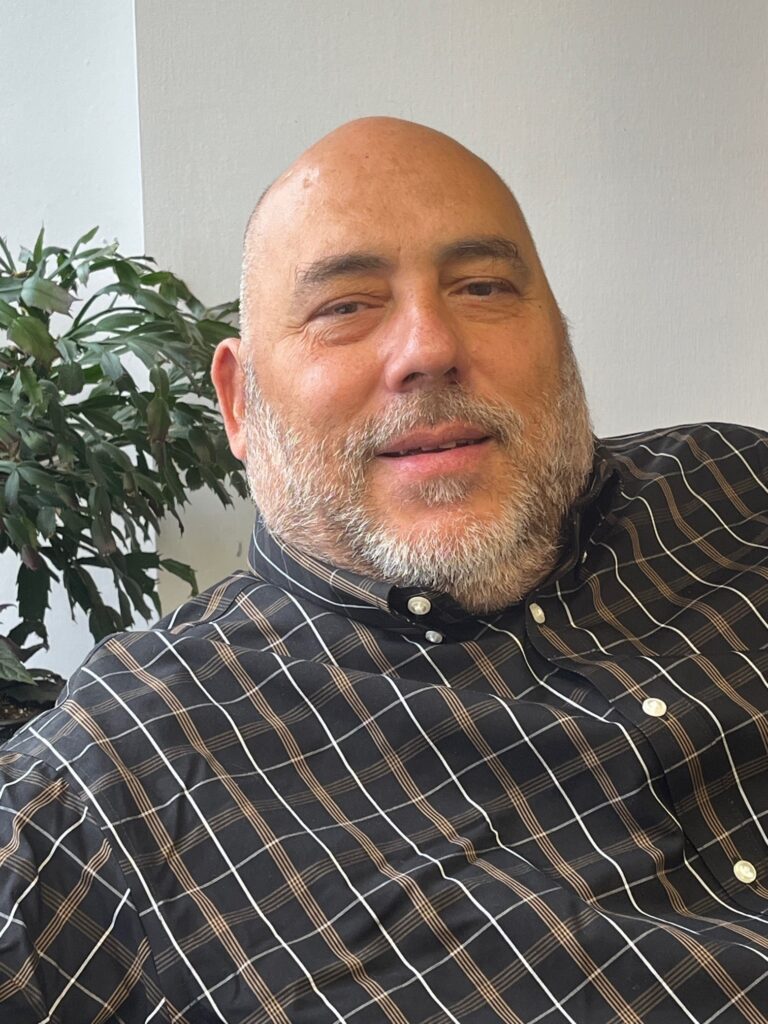 LIFTT Executive Director Carlos Ramalho, A bald white hispanic man with a gray beard wearing a black, white and gold plaid shirt