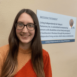PCA program assistant Kasey Mook. A white woman with dark hair wearing glasses and a two tone orange sweater