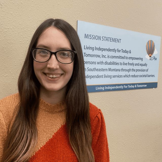 white woman with dark hair wearing glasses and a two tone orange sweater