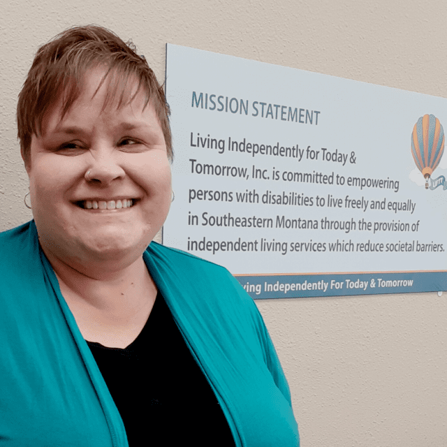 white female with short blond hair wearing a green sweater and black shirt