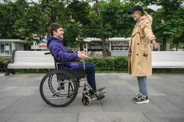 A joyful couple in a park, featuring a man in a wheelchair and a woman in a coat, sharing a moment. (Stock Photo/SHVETS Productions)